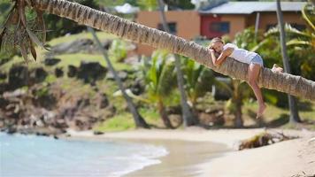 aanbiddelijk weinig meisje zittend Aan palm boom gedurende zomer vakantie Aan wit strand video