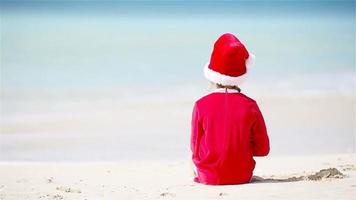 vista traseira da adorável garota com chapéu de natal na praia branca durante as férias de natal video