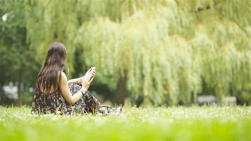 süße Frau liest SMS auf dem Handy, während sie im Park sitzt. video