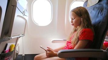 Adorable little girl traveling by an airplane. Kid listening music sitting near aircraft window video