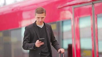 Young caucasian man with smarphone and luggage at station traveling by train video