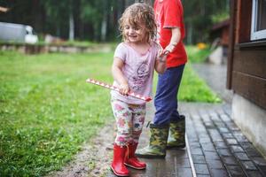 brother and sister play in rainy weather Children jump in puddle and mud in the rain. photo