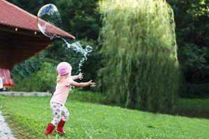 happy girl playing with soap bubbles outdoor. A little girl pops a soap bubble photo