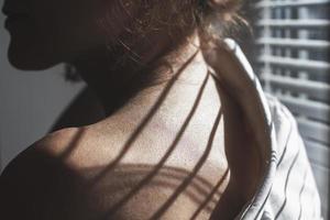 Sensual close up portrait of beautiful young lady relaxing at the window. female shoulder close up. hard shadows photo