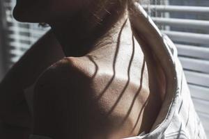 Sensual close up portrait of beautiful young lady relaxing at the window. female shoulder close up. hard shadows photo