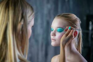 mujer aplica maquillaje a el cara de un bonito joven modelo foto