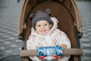 alegre pequeño bebé sentado en un paseante al aire libre foto