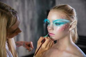 mujer aplica creativo maquillaje a el cara de un joven modelo foto