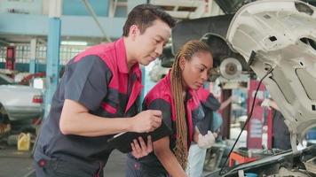 Masculin professionnel automobile superviseur et noir femelle collaborateur discuter et inspecter réparation travail listes de contrôle à voiture garage, un service entretien, et fixation spécialiste métiers auto industrie. video