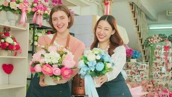 Two cheerful female florist workers give beautiful flora bouquets and look at camera together, happy and bright smiles, arranging work in a colorful flower shop, SME business entrepreneur people. video