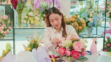 un Jeune magnifique asiatique femelle fleuriste ouvrier organiser et décorer bouquet de Frais fleurs, Valentin ordres, souriant avec content travail dans coloré Ralentissez boutique, petit affaires pme entrepreneur.