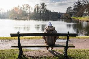 contemplación por el lago. un joven mujer sentado en un parque banco foto