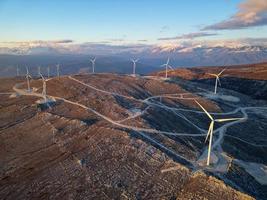 molinos de viento en las colinas durante la puesta de sol. energía renovable, energía verde. montañas en el fondo con nieve. energía eólica y respetuoso con el medio ambiente. Futuro sostenible. acabar con los combustibles fósiles. foto