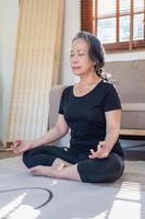 Asian elderly woman meditating practicing yoga for good health At an older age, it's about taking care of your body's health at home on a relaxing day. good health concept photo