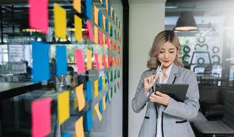 secretaria que trabaja en una oficina moderna en rascacielos, escribiendo y pegando notas adhesivas con tareas en la oficina moderna de la ventana foto