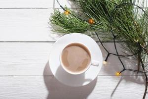 Christmas latte coffee on a white wooden table with pine tree and lights decor. winter holiday morning. top view photo