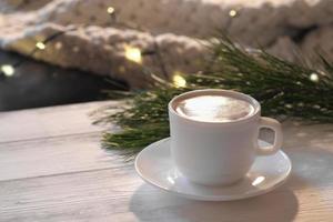 Christmas latte coffee on a white wooden table with pine tree and bokeh lights decor. cozy winter holiday morning. front view. photo