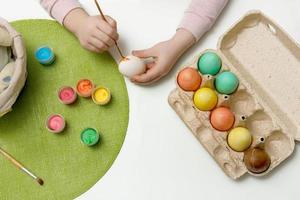 niño pinturas huevos con vistoso pinturas y pone ellos en un cesta, Pascua de Resurrección contenido foto