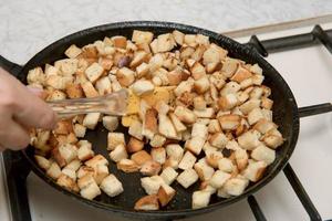 female hand stirs crackers fried in a frying pan photo