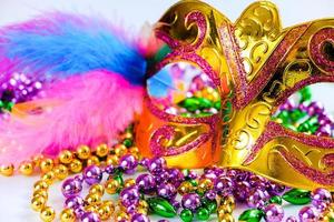 Golden carnival mask and colorful beads on white background. Closeup symbol of Mardi Gras or Fat Tuesday. photo