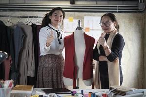 gente del equipo de moda, diseñadora asiática y asistente adolescente en el estudio, pulgar hacia arriba y sonrisa, feliz trabajando con hilo y costura para el diseño de vestidos, empresaria profesional de sastrería boutique. foto