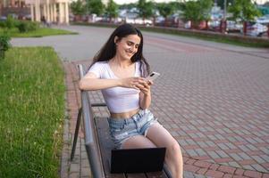 un joven niña es sentado en un banco y hablando en el teléfono foto