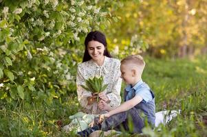 mamá es sentado siguiente a su hijo en el césped , el chico es participación flores en su manos foto