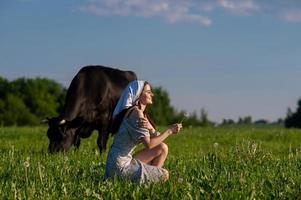 A young girl in a cow pasture is sitting with her eyes closed in a dress photo