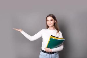 un linda estudiante niña sostiene cuadernos para notas y puntos a el lado con su mano foto