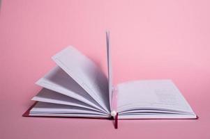 An open notebook with a pen, lying on a pink background photo