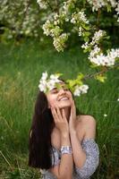 The girl is standing under a tree with her eyes closed. White petals are falling on the face photo