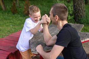 un linda niño pruebas el fuerza de su manos con su papá. levantamiento de pesas foto