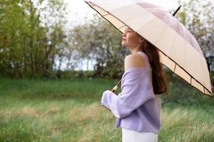 A girl in a sweater is standing under an umbrella. it's raining photo