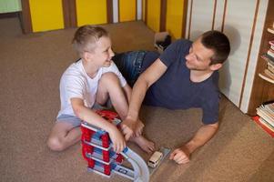 Cheerful dad plays with a cute boy at home in cars photo