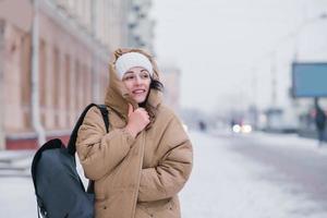 A cute girl in a coat and hat walks around the city in bad cold weather, hiding from the wind photo