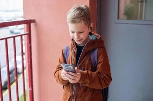 A cute boy is standing with a backpack and a phone with headphones photo