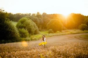 A girl runs through a field with spikelets against the background of the setting sun photo