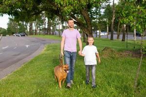 un alegre papá sostiene el mano de un emocional hijo. un perro en un Correa. foto