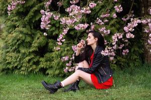 A young girl in a black jacket and a red dress is sitting next to sakura photo