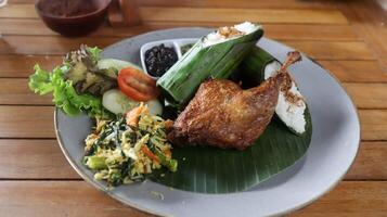 Crispy black fried duck with rice covered in banana leaf, some vegetable and special mash chili. photo