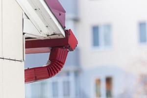 A drop of melting snow on the red roof gutter of a building against the background of a house. Photo in high quality. Horizontal.