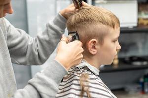 un chico es sentado en un Barbero comercio, corte su pelo con un clíper foto