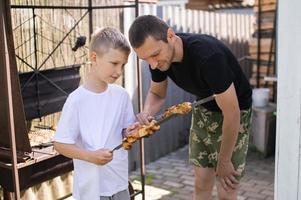 gracioso papá y hijo tratar A la parrilla carne foto