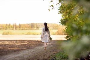 A cute girl in a white long dress stands in spring on a yellow rapeseed field photo