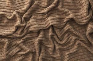 Brown crumpled knitted scarf or sweater texture, top view. Texture background of warm crocheted clothing textile. Knitwear fabric. photo