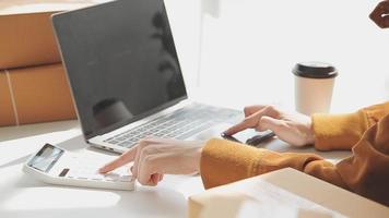 mujer de negocios asiática en el sofá usando una computadora portátil revisando las cajas de envío en línea del pedido del cliente en casa. Emprendedor autónomo de pequeña empresa pyme. negocio en línea, concepto de hogar de trabajo de pyme. video