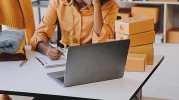 Moda diseñador l joven asiático mujer trabajando utilizando computadora portátil, tableta y sonriente mientras en pie en taller respondiendo en negocio video