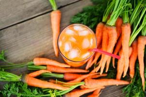 jugo de zanahoria en el fondo de la mesa de madera, rodajas de zanahoria frescas y dulces para cocinar frutas y verduras para el concepto de salud, jugo de zanahoria fresco en vidrio con hielo en verano foto