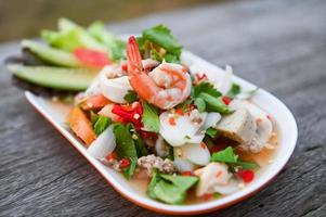 mixed salad with shrimp squid pork sausage with fresh vegetable cucumber celery leaf on plate on wooden table - Thai food salad photo