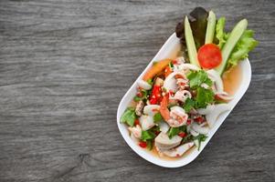 mixed salad with shrimp squid pork sausage with fresh vegetable cucumber celery leaf on plate on wooden table, Thai food salad photo